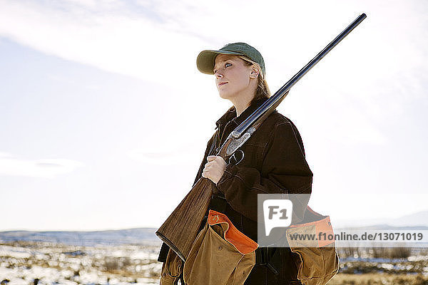Woman looking away while holding rifle against sky