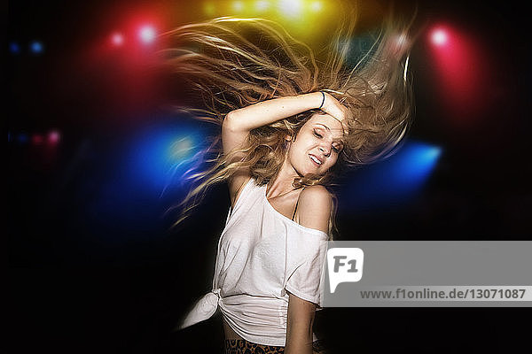 Frau mit blonden Haaren tanzt auf Gartenparty gegen beleuchtete mehrfarbige Lichter