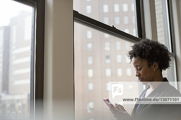Geschäftsfrau benutzt Telefon  während sie im Büro am Fenster steht