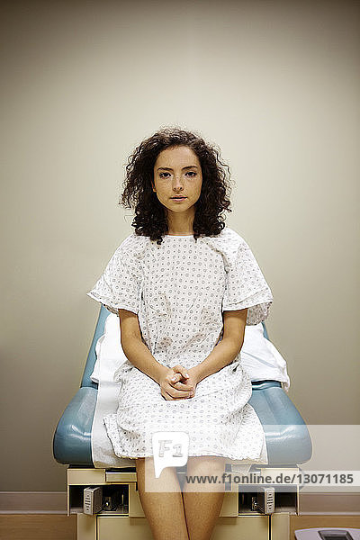 Portrait of woman with hands clasped sitting on bed in hospital