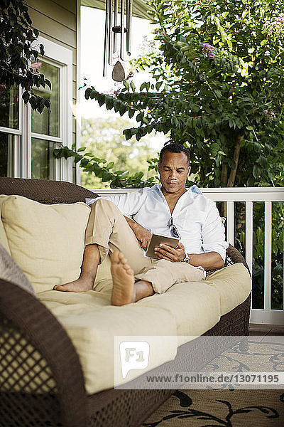 Mann benutzt Tablet-Computer  während er sich auf dem Sofa in der Veranda entspannt