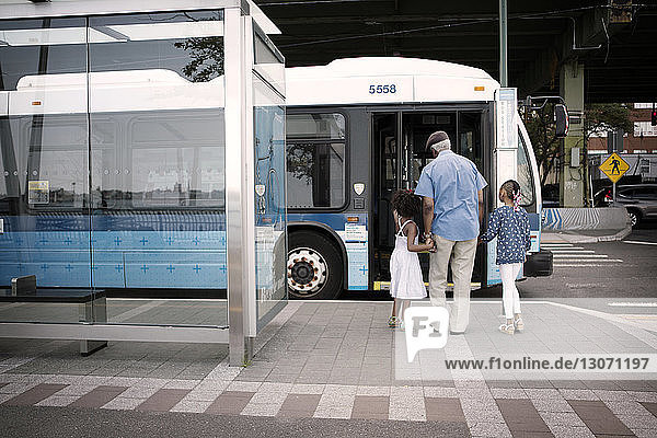 Rückansicht von Großvater und Enkelkindern  die in der Stadt auf den Bus zugehen