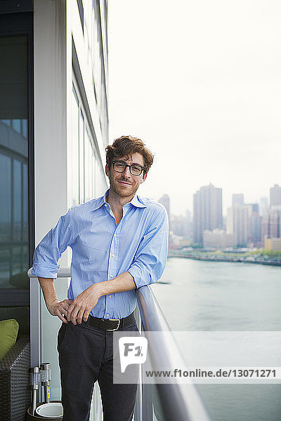 Portrait of smiling businessman leaning on railing at office balcony