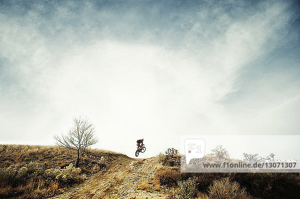 Man riding motorcycle on dirt road against sky