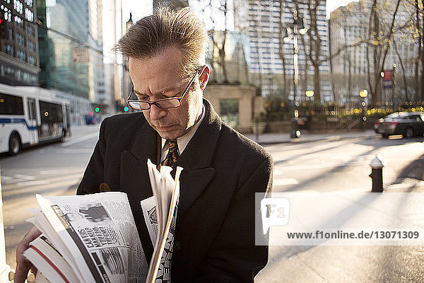 Businessman reading newspaper while standing on footpath