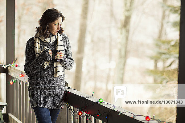Thoughtful woman with coffee cup looking away while standing by railing