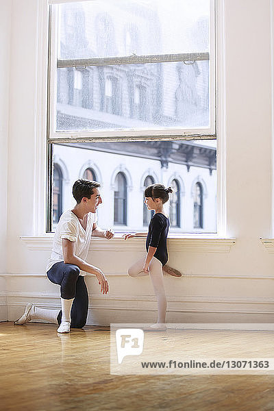 Seitenansicht eines männlichen Ballettlehrers im Gespräch mit einer Ballerina am Fenster im Studio