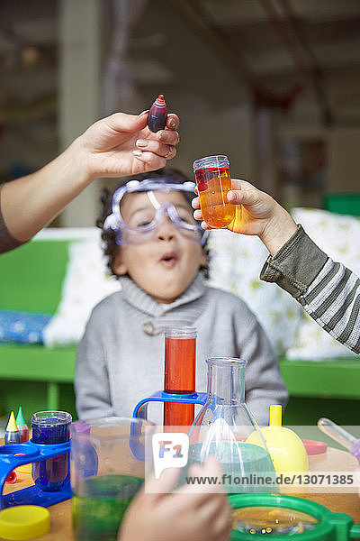 Erstaunter Junge schaut Lehrer und Freund an  der in der Vorschule ein wissenschaftliches Experiment macht
