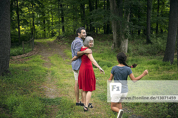 Mädchen rennt auf Großmutter und Vater zu  auf einem Pfad zwischen Bäumen im Wald