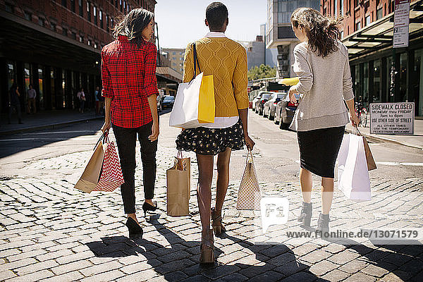 Rückansicht von Frauen mit Einkaufstaschen beim Spaziergang auf der Straße