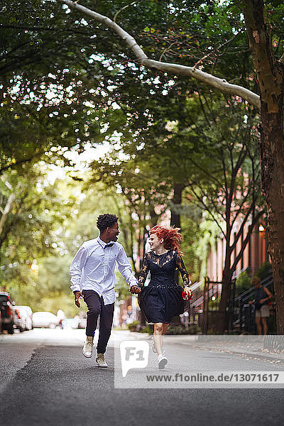 Happy couple holding hands and running on street