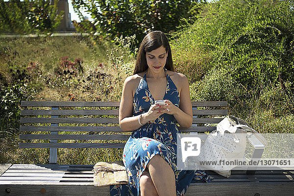 Frau benutzt Smartphone  während sie im Park auf einer Bank sitzt