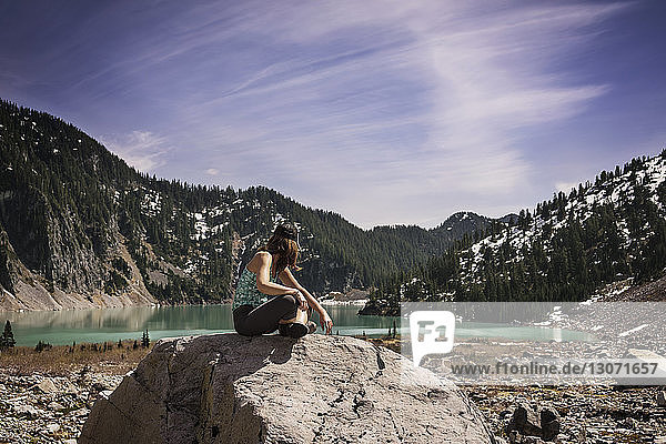 Side view of woman sitting on rock against mountain