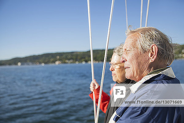 Seitenansicht eines nachdenklichen älteren Paares auf einer Yacht auf See vor klarem Himmel