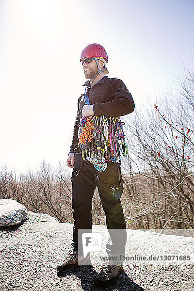Man with hiking equipment looking away while standing on rocks against clear sky