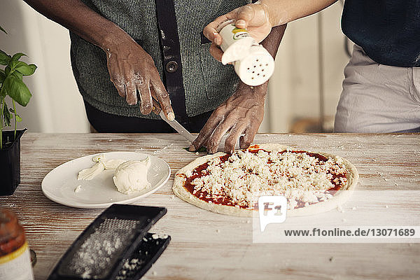 Midsection of couple preparing pizza while standing at kitchen table