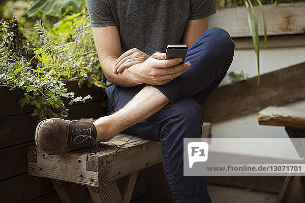 Niedriger Teil des Mannes benutzt ein Smartphone  während er auf einer Bank sitzt