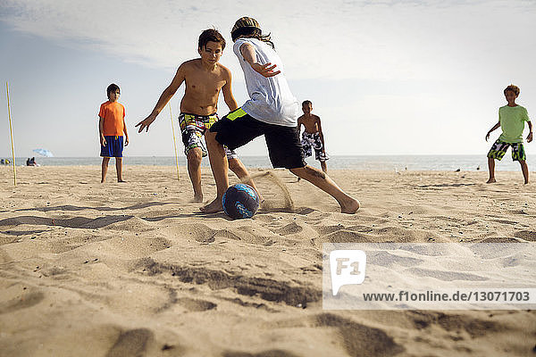 Friends playing soccer at beach against sea