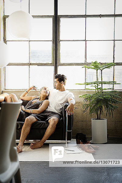 Couple talking while resting on sofa against window at home
