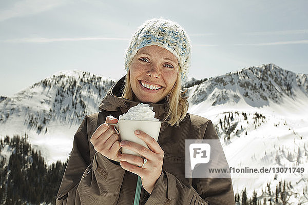 Portrait of woman holding whipped cream while standing against snowcapped mountain
