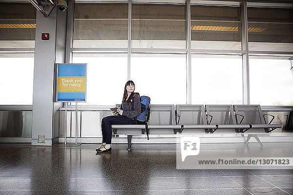 Frau mit Tablet-Computer schaut weg  während sie auf Sitzen im Warteraum des Bahnhofs sitzt