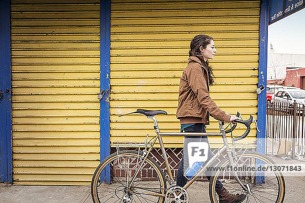 Seitenansicht einer Frau mit Fahrrad auf einem Fußweg in der Stadt