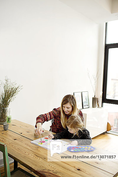 Hochwinkelansicht von Mutter und Tochter beim Malen  während sie zu Hause am Tisch sitzen