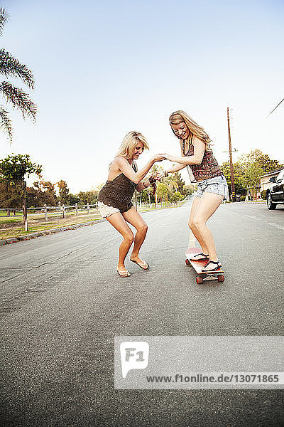 Friends playing with skateboard on road against clear sky