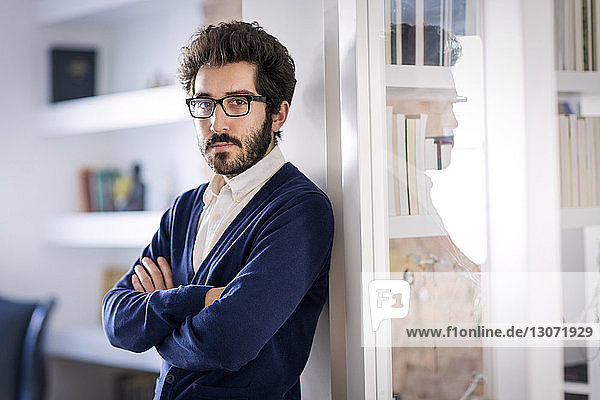Portrait of confident man with arms crossed leaning on wall at home