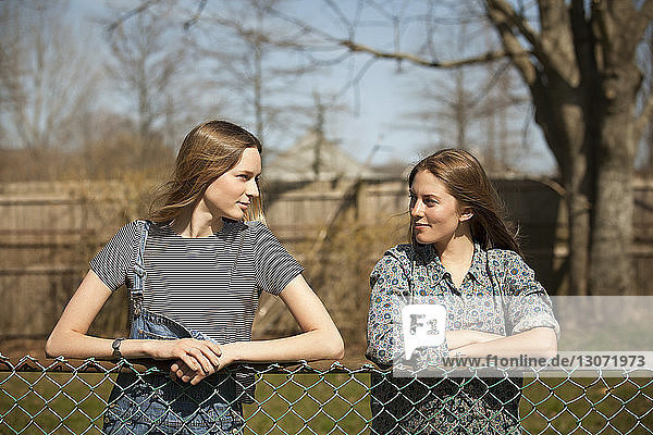 Friends talking while standing by chainlink fence in park