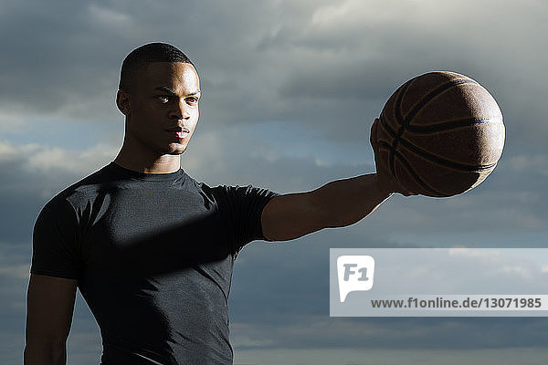Selbstbewusster Sportler mit Basketball gegen bewölkten Himmel