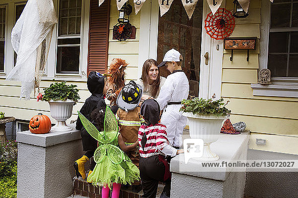 Frau spricht mit Kindern in Halloween-Kostümen während eines Streiches oder einer Behandlung