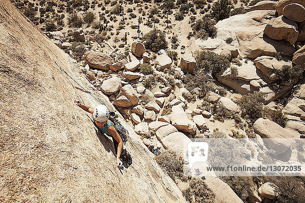 Hochwinkelaufnahme einer Frau  die an einem sonnigen Tag an einer Felsformation klettert