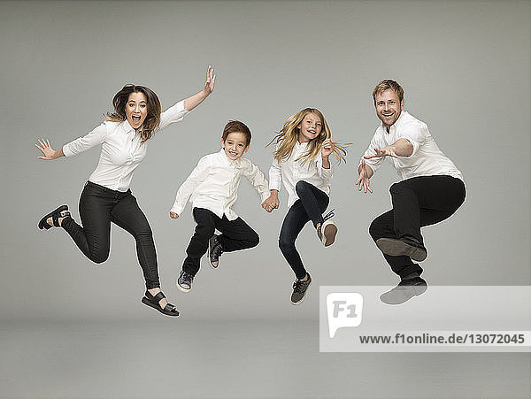 Porträt einer spielerischen Familie beim Springen vor grauem Hintergrund