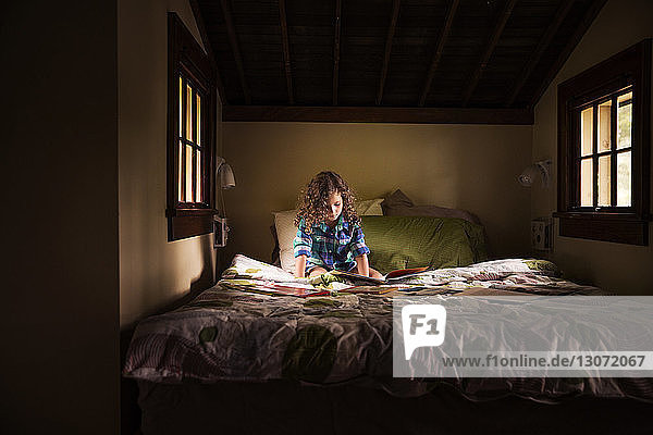 Girl reading book while sitting on bed in cabin