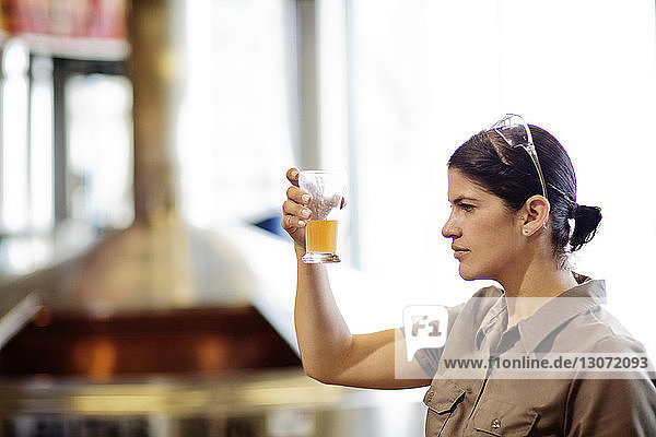 Woman examining beer in glass beaker while standing at brewery