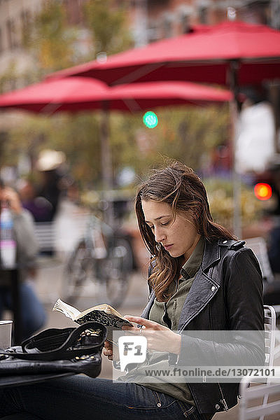 Frau liest Buch  während sie am Tisch im Straßencafé sitzt