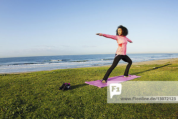 Frau  die eine Krieger-2-Yoga-Pose auf Feld gegen Meer praktiziert