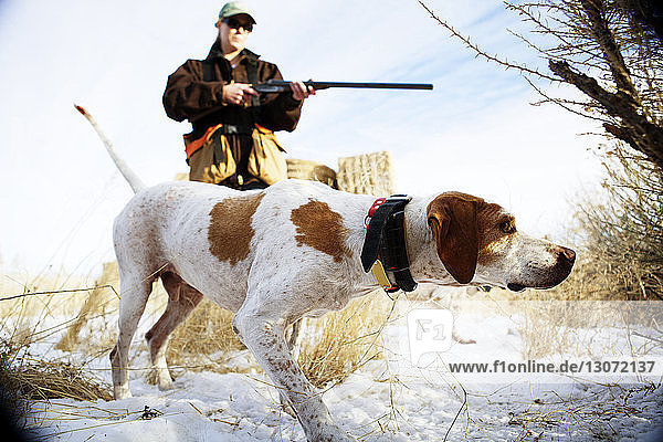 Woman holding rifle while standing with dog on snow covered field