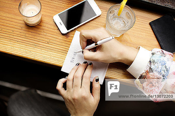 Beschnittenes Bild einer Frau  die auf Seidenpapier schreibt  während sie in einer Bar sitzt