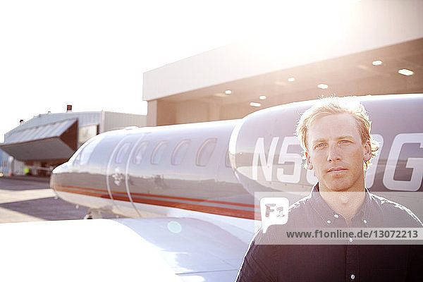 Porträt eines Mannes  der am Hangar gegen ein Flugzeug steht