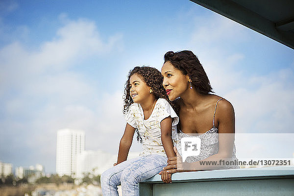 Mutter und Tochter schauen weg  während sie sich am Geländer am Pier gegen den Himmel entspannen