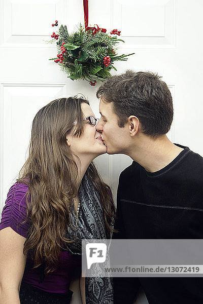 Couple kissing while standing against door at home