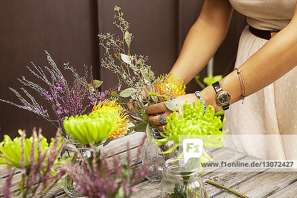 Cropped image of woman arranging flowers in jars on wooden table