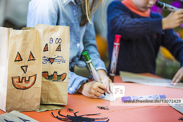 Smiley-Gesichter auf Papiertüten von Geschwistern  die während der Halloween-Party Kunst bei Tisch machen