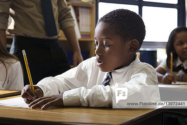 Junge schreibt während des Unterrichts im Klassenzimmer auf Papier