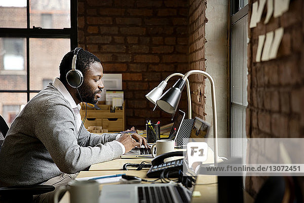 Seitenansicht eines Geschäftsmannes  der während seiner Arbeit im Büro Musik hört