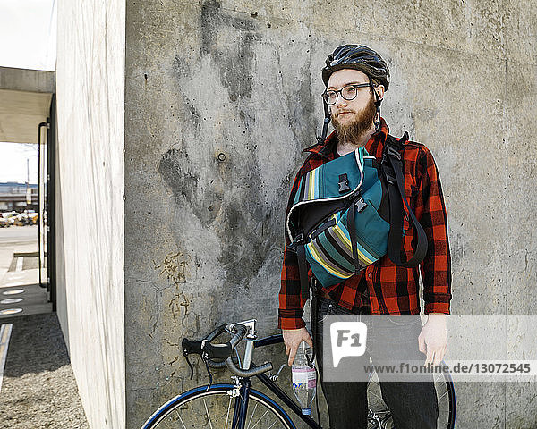 Man with bicycle looking away while standing against building