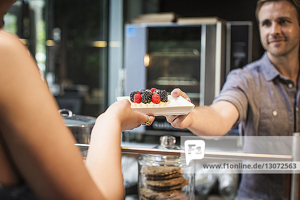 Smiling owner serving tart to woman at coffee shop
