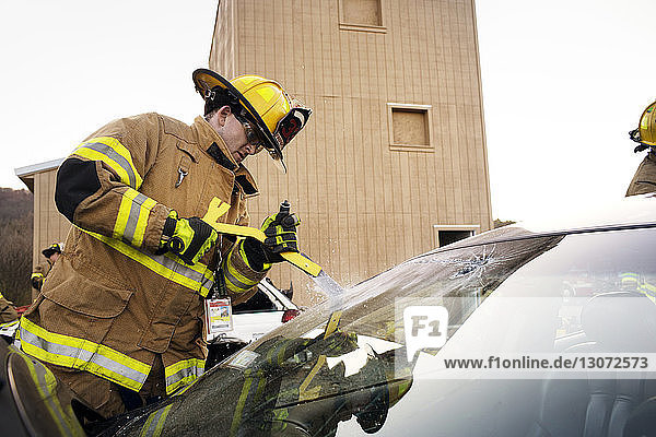 Feuerwehrmann schneidet Windschutzscheibe eines Autos auf  während er am Haus steht